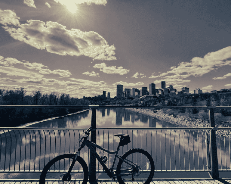 Cyclist riding a paved multi-use trail through Edmonton's North Saskatchewan River valley in summer